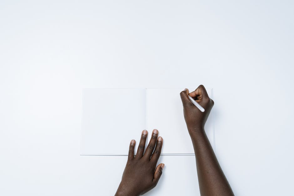 A person holding a pen, writing on a blank paper notebook, symbolizing the creation of a personalized professional development plan.